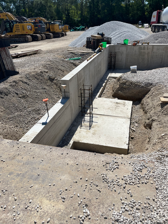 Construction site with concrete foundation and retaining wall; gravel, excavation equipment.