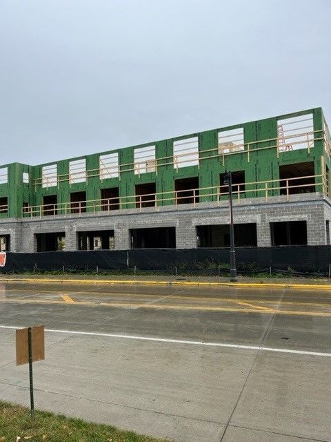 Building under construction with wood framing and gray block facade. Black fence in front.