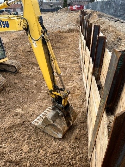Yellow excavator digging a trench next to a shoring wall on a construction site.