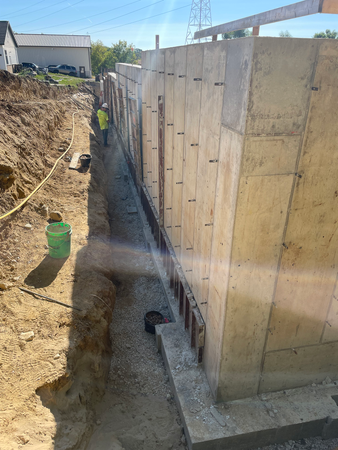 Construction of a concrete retaining wall with a worker in the trench, sunny day.