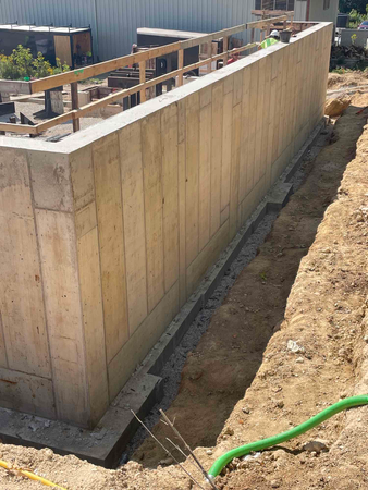 Concrete foundation wall under construction, with a trench and exposed rebar.