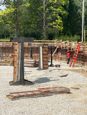 Construction site with concrete forms, gravel, and a worker by a ladder.