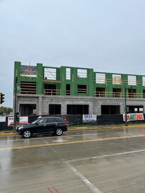 Building under construction with green framing, gray brick, and a black car on a wet street.