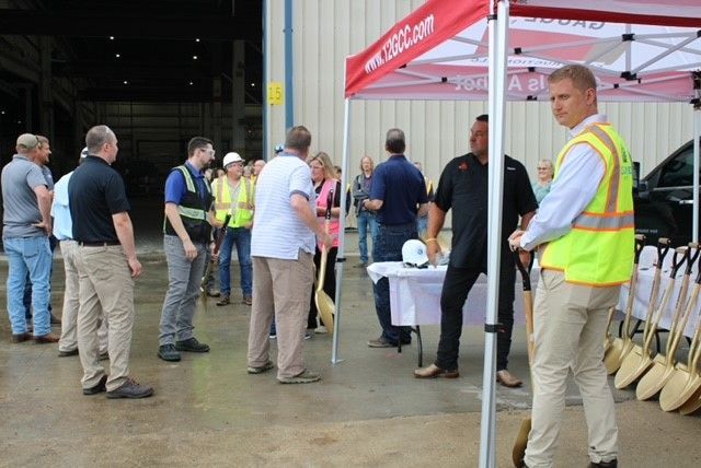 Group of people at an outdoor event with shovels, a white table, and a red tent. Some wearing vests.