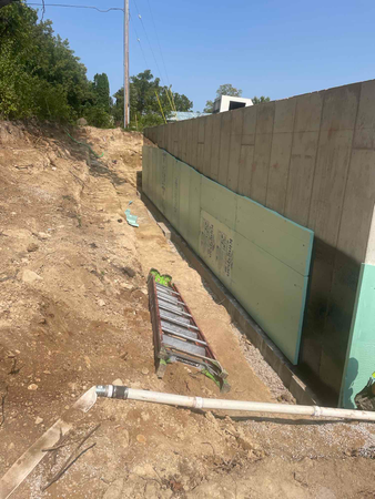 Construction site with an insulated concrete wall, soil, ladder, and drainage pipes.