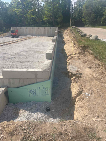 Construction site with foundation walls, gravel, and an excavation trench alongside.