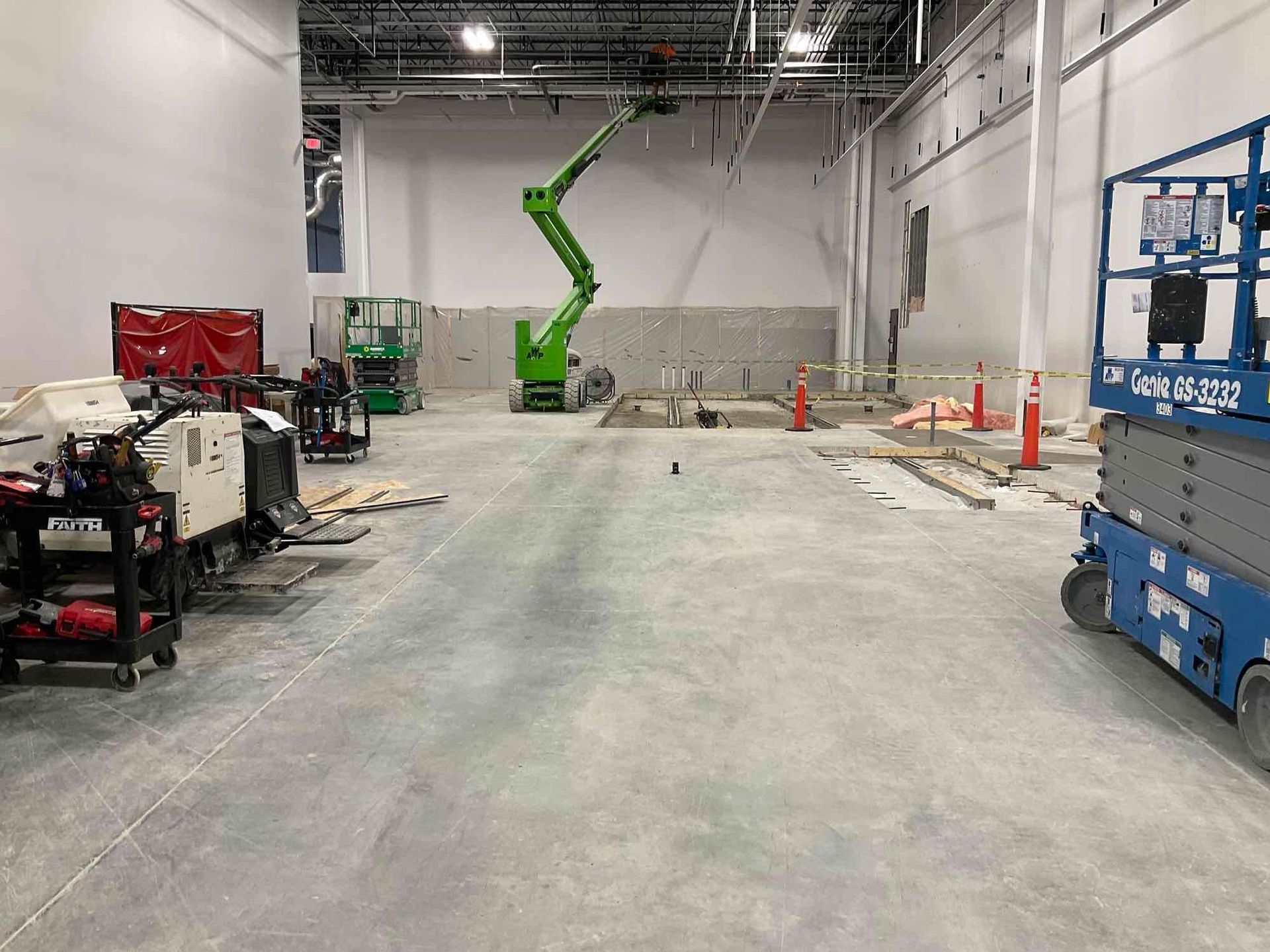 Construction site with concrete floor, walls, and machinery. Green lift and blue scissor lift present.
