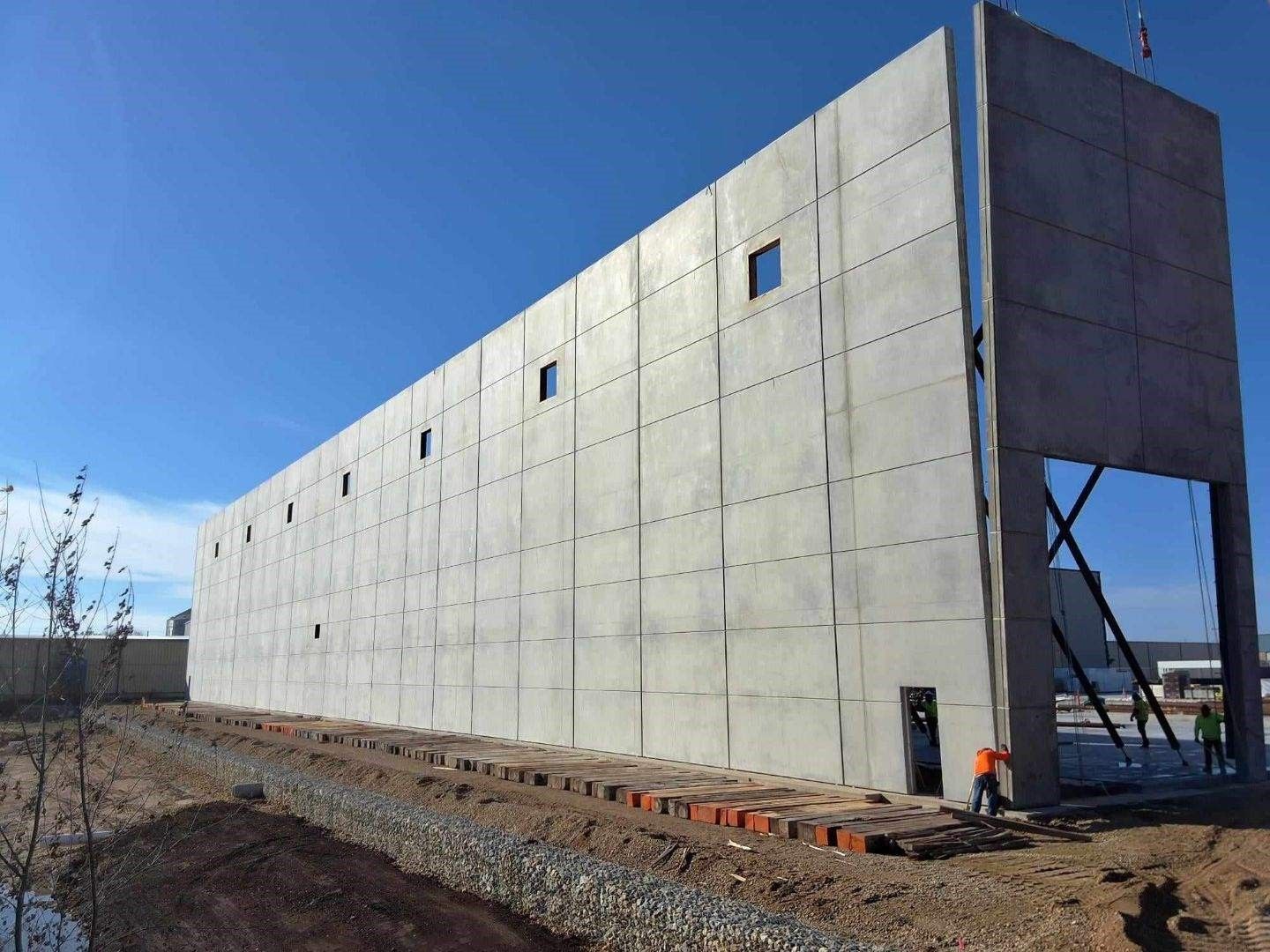 Large concrete building under construction; workers in orange vests near an opening.