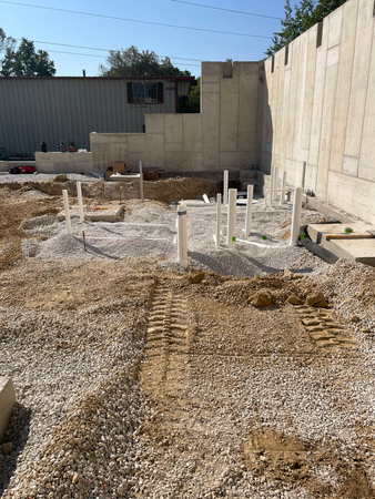 Construction site with plumbing pipes set in gravel. Concrete walls and building in the background.