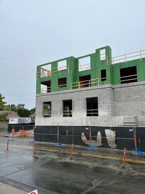 Construction site, building in progress. Wooden frame atop gray block structure, fenced perimeter.