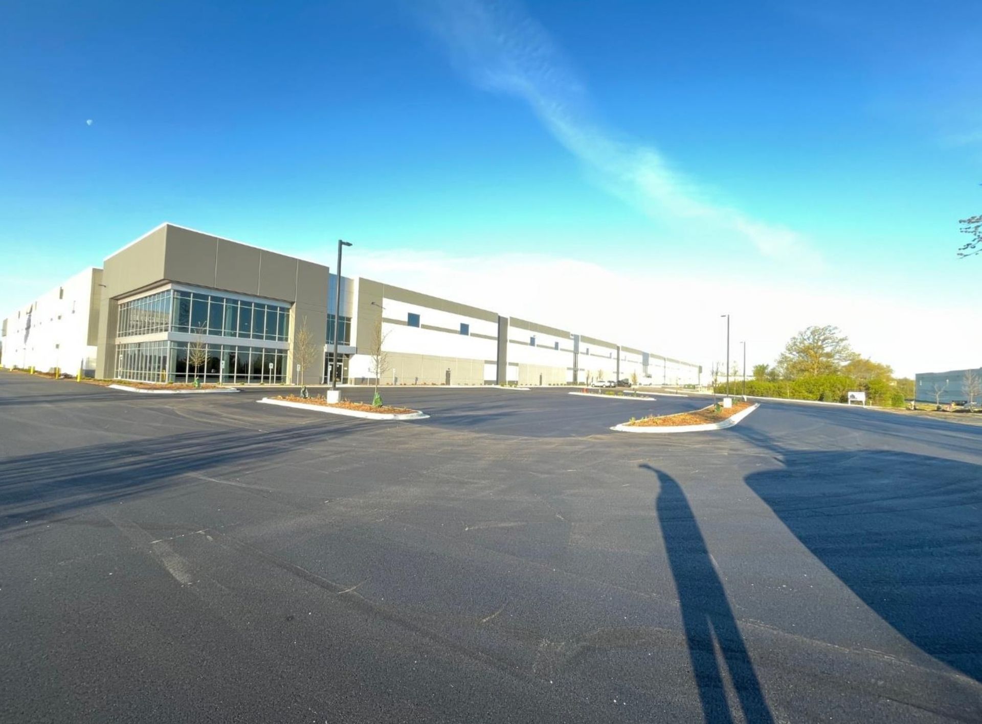 Empty parking lot beside a modern industrial building under a clear blue sky