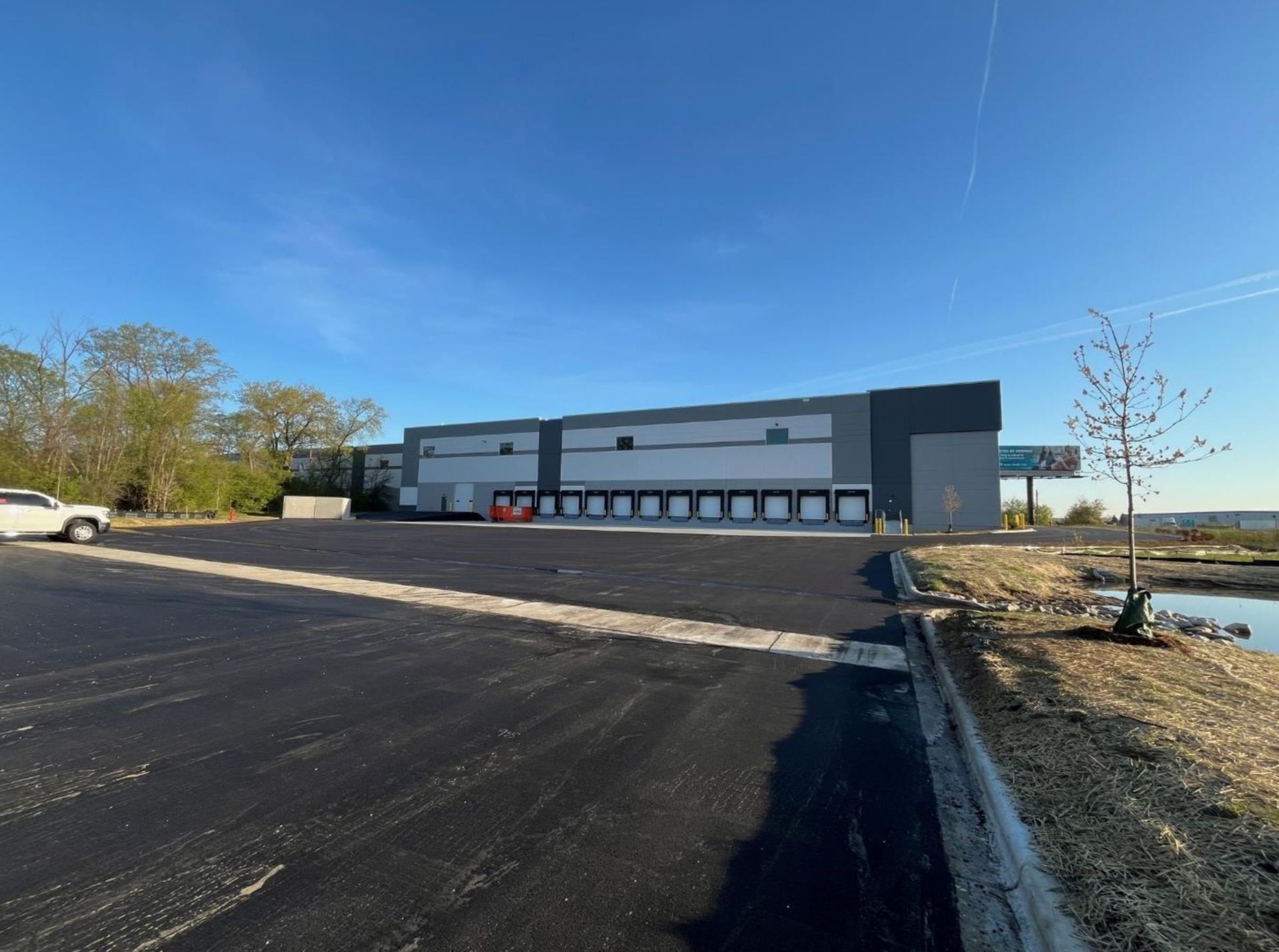 Exterior of a large gray warehouse with a black paved lot under a clear blue sky