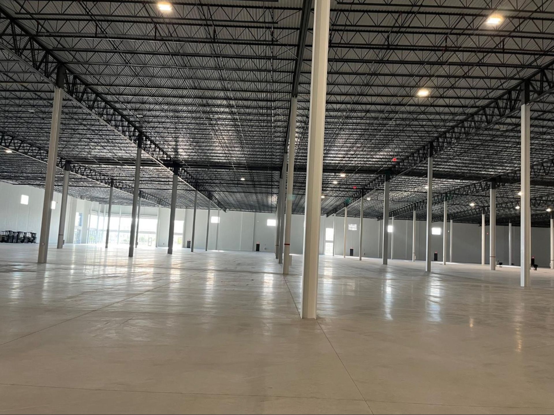 Empty warehouse interior with polished concrete floor, exposed steel beams, and rows of white support columns
