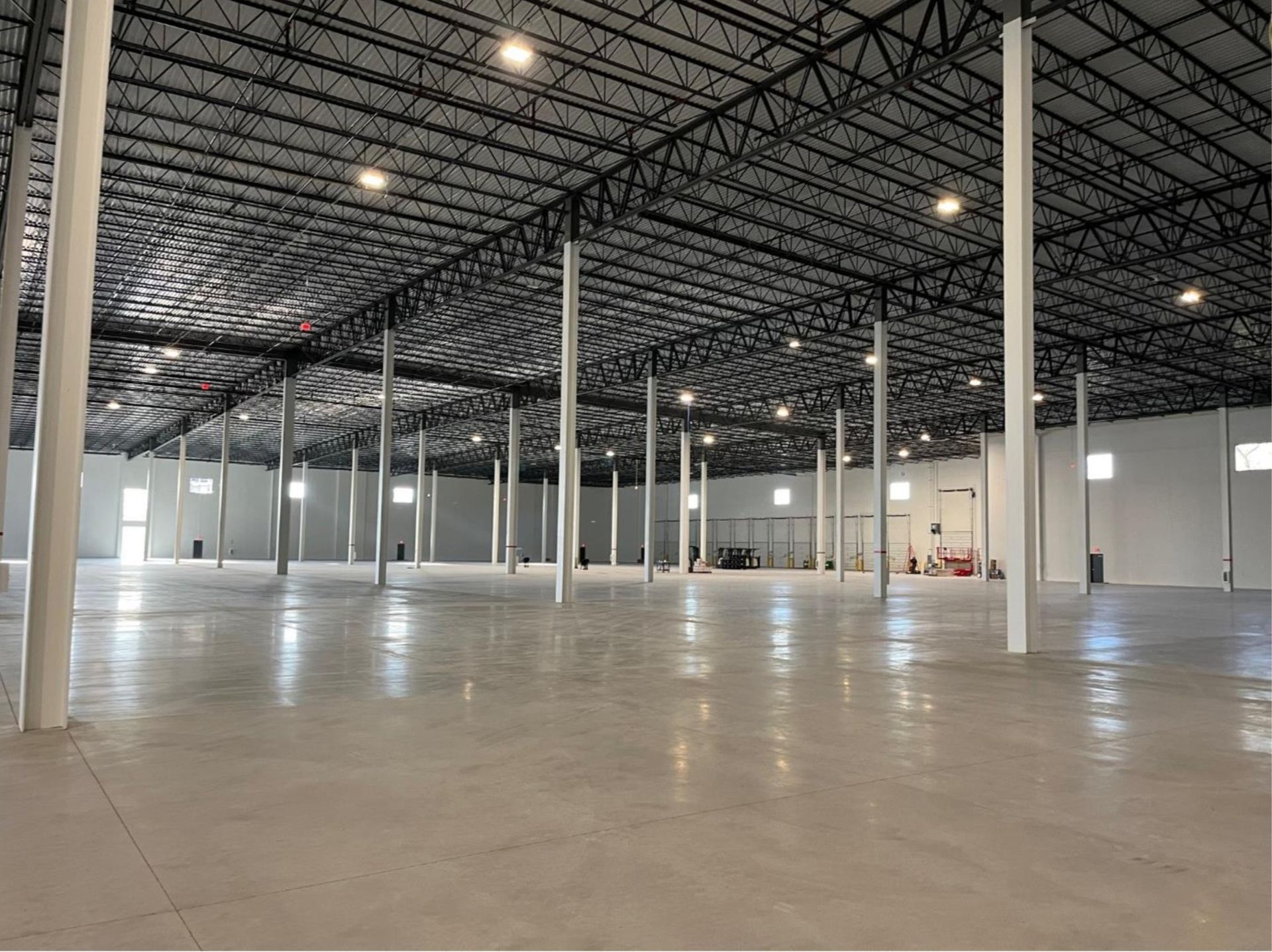Empty industrial warehouse with high ceilings, white columns, and a polished concrete floor