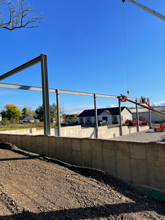 Construction site: Steel beams erected, worker in lift, blue sky.