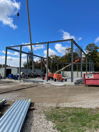 Steel framework of a building under construction, with cranes and lift equipment on a concrete foundation, outdoors.