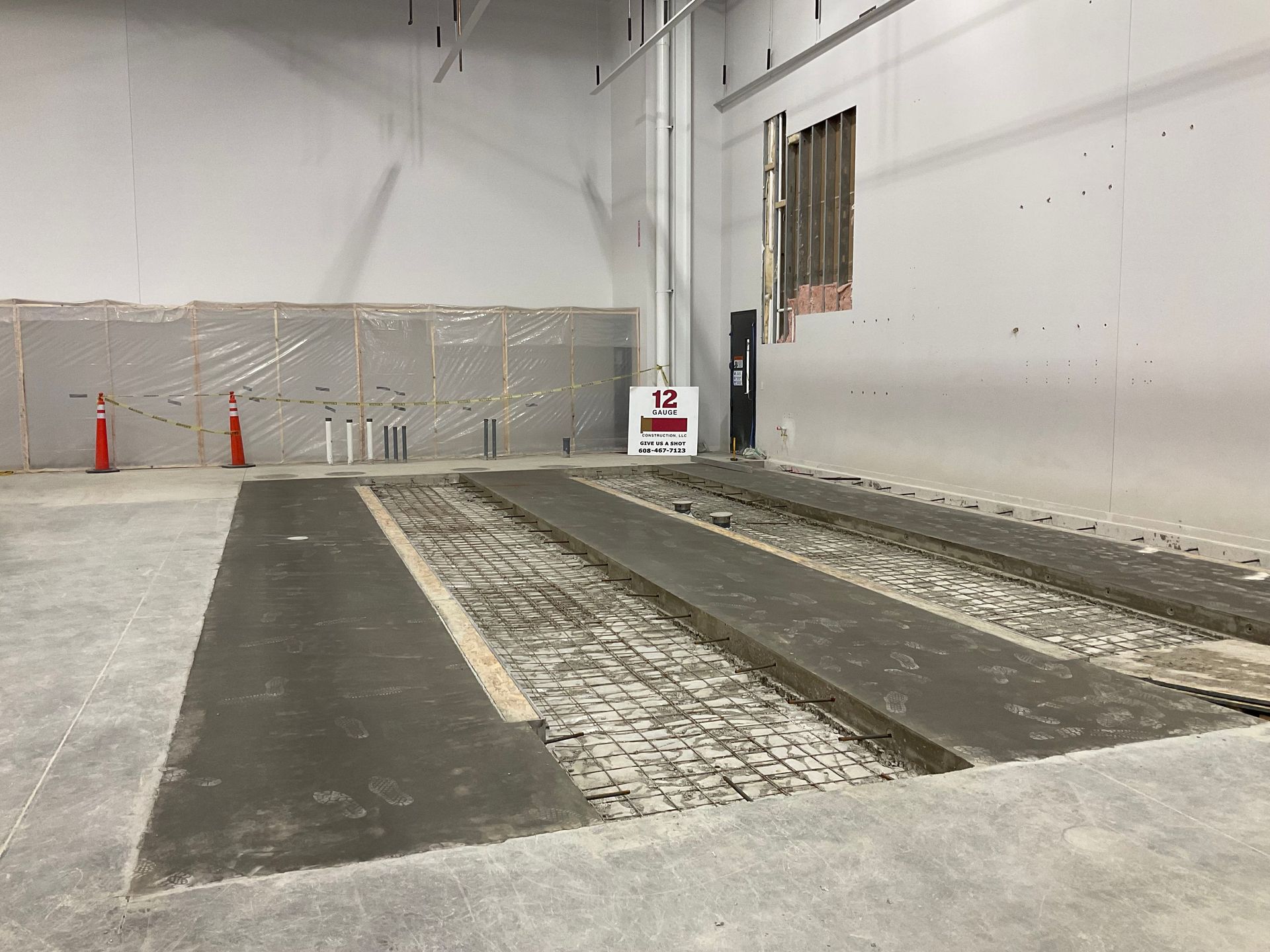 Three recessed vehicle service bays in a concrete floor. Gray walls, a window, and some construction materials are visible.