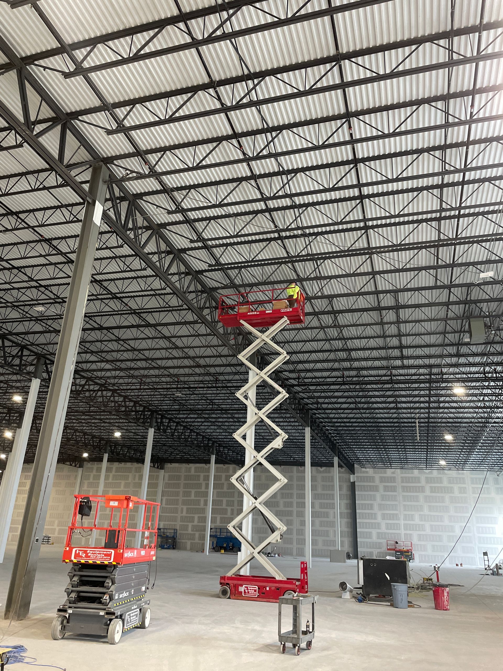 Scissor lift raised high inside a warehouse with a red basket near the ceiling