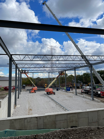 Steel frame building under construction, with lift equipment against a cloudy sky.