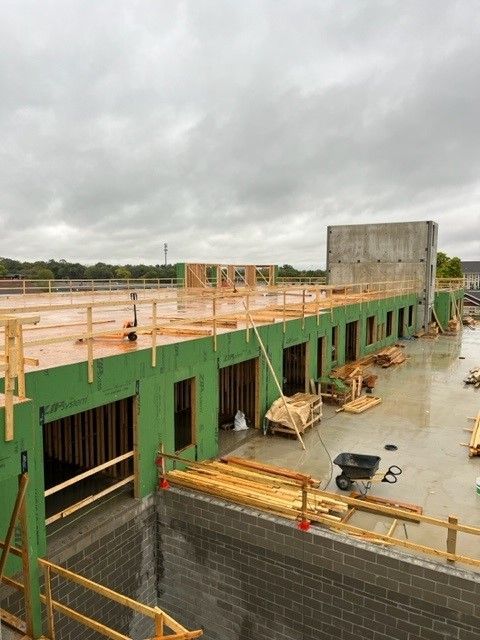 Building under construction with green exterior, wooden framing, and gray block walls under a cloudy sky.