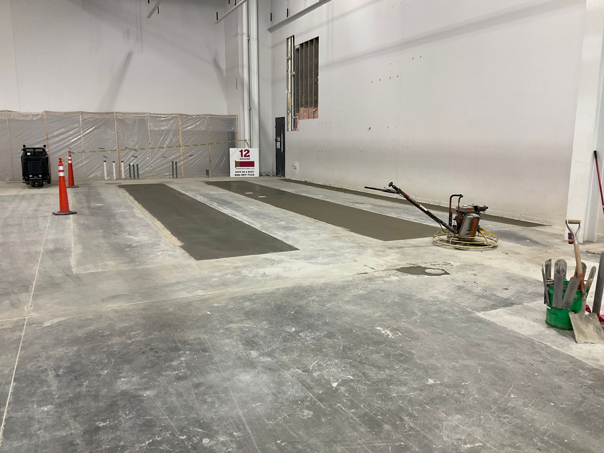 Concrete work in progress indoors, with strips of wet concrete and tools.