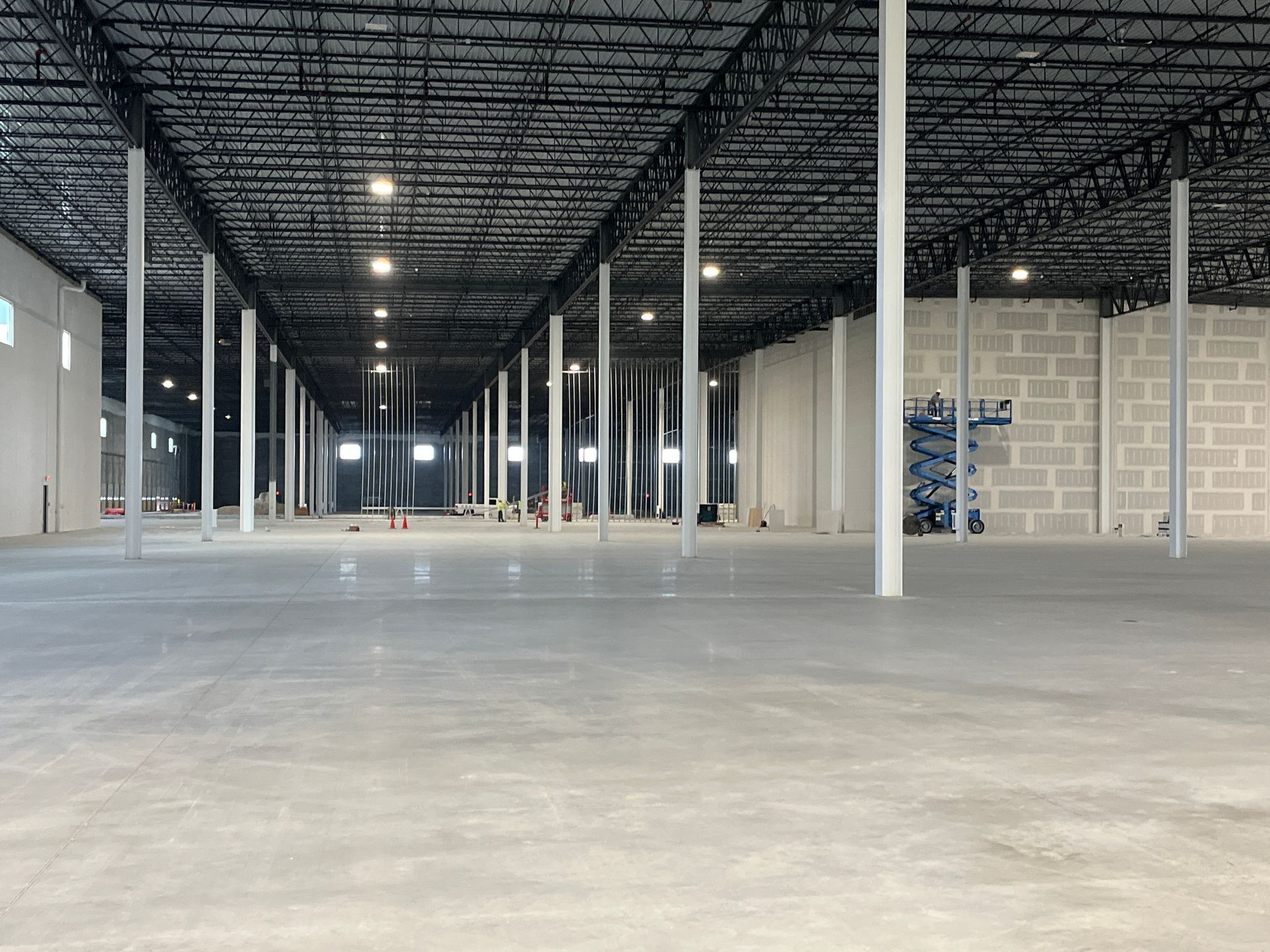 Empty industrial warehouse with concrete floor, exposed ceiling, and rows of white columns