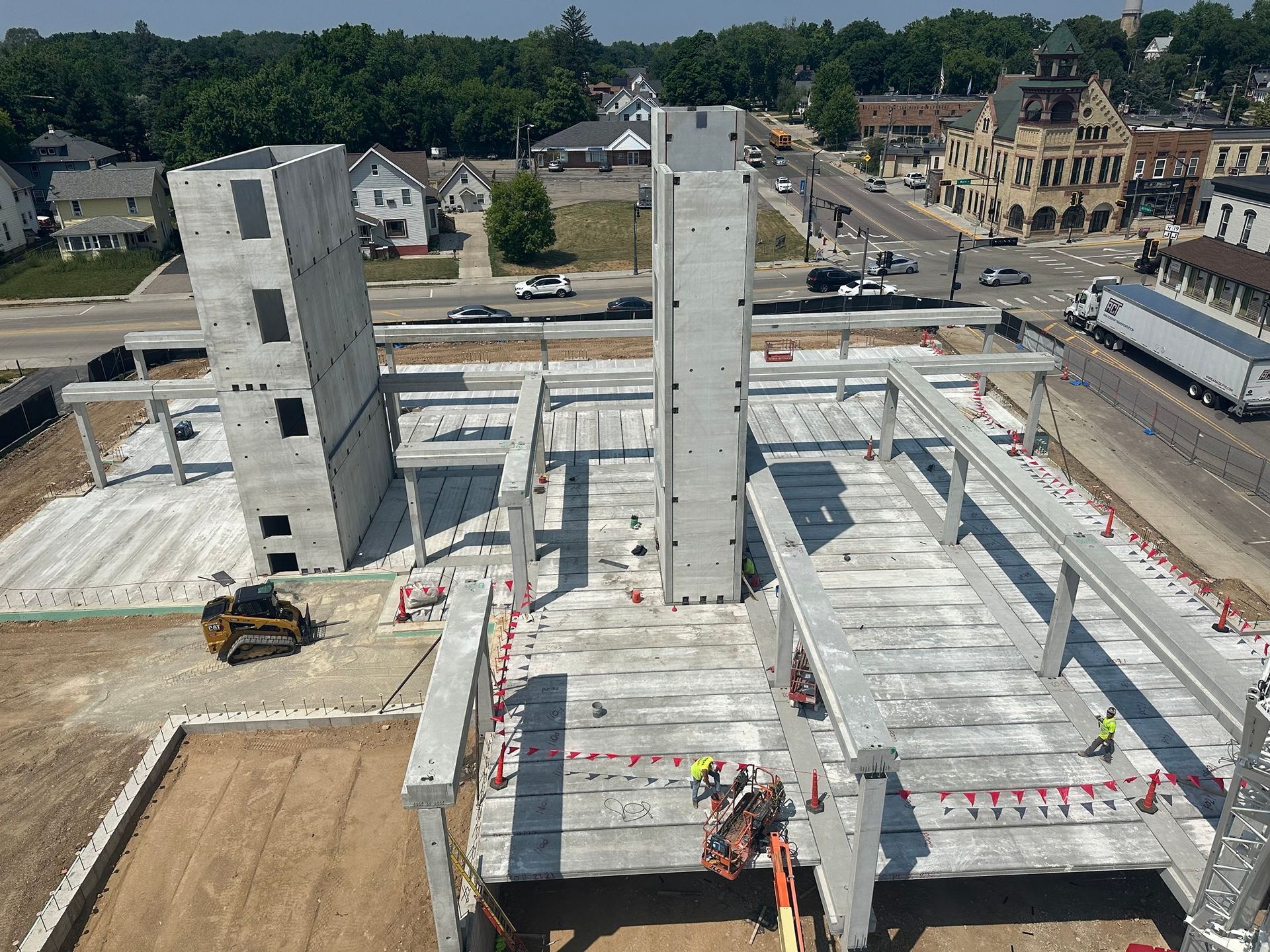 Construction site with precast concrete building components; heavy equipment, road with traffic, sunny day.