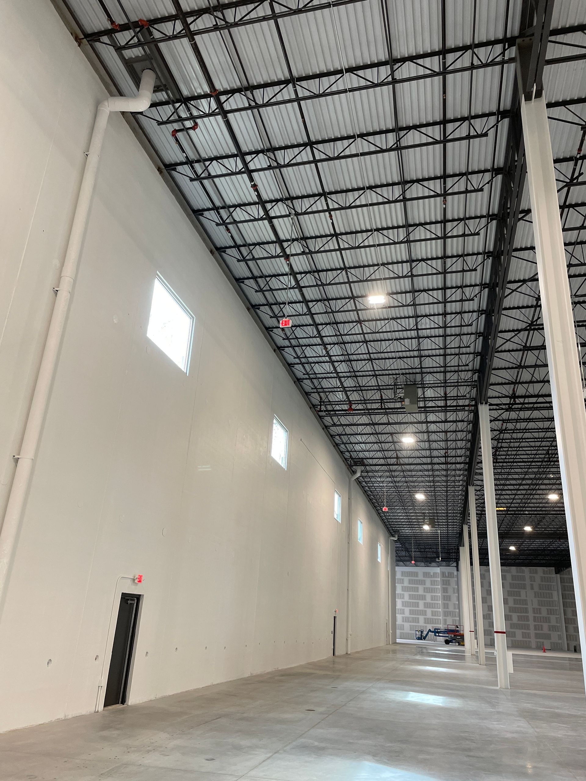 Empty industrial warehouse with high ceiling, exposed beams, white walls, and polished concrete floor