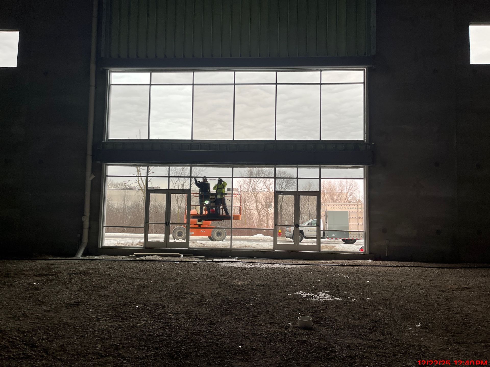 Workers on lift installing glass windows in a large industrial building.