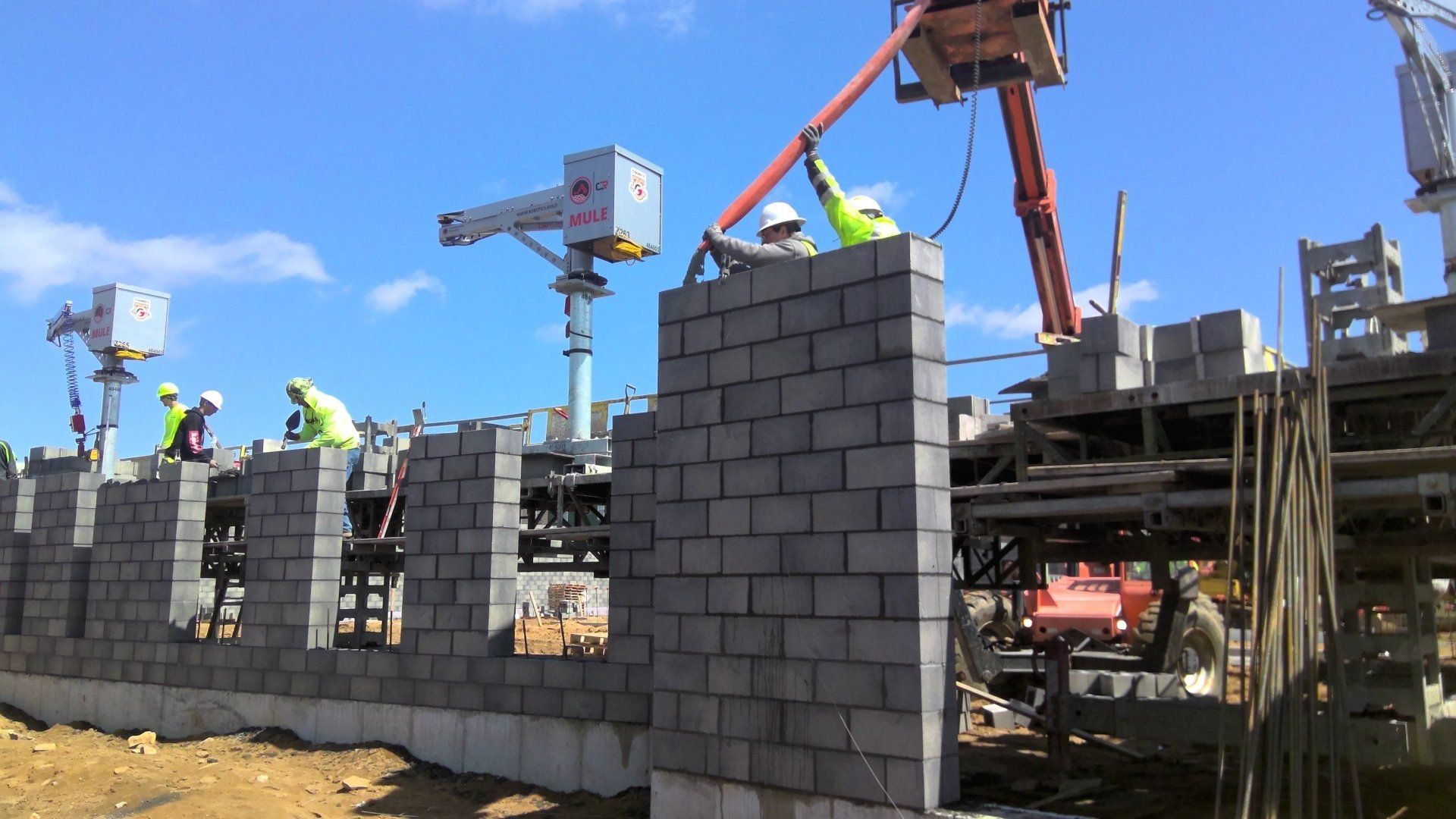Construction workers building a concrete block wall using crane and lift. Bright blue sky.