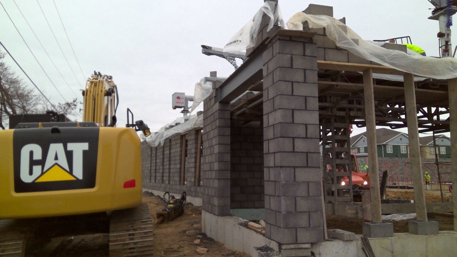 Construction site with a backhoe, concrete block wall, and exposed roof beams.