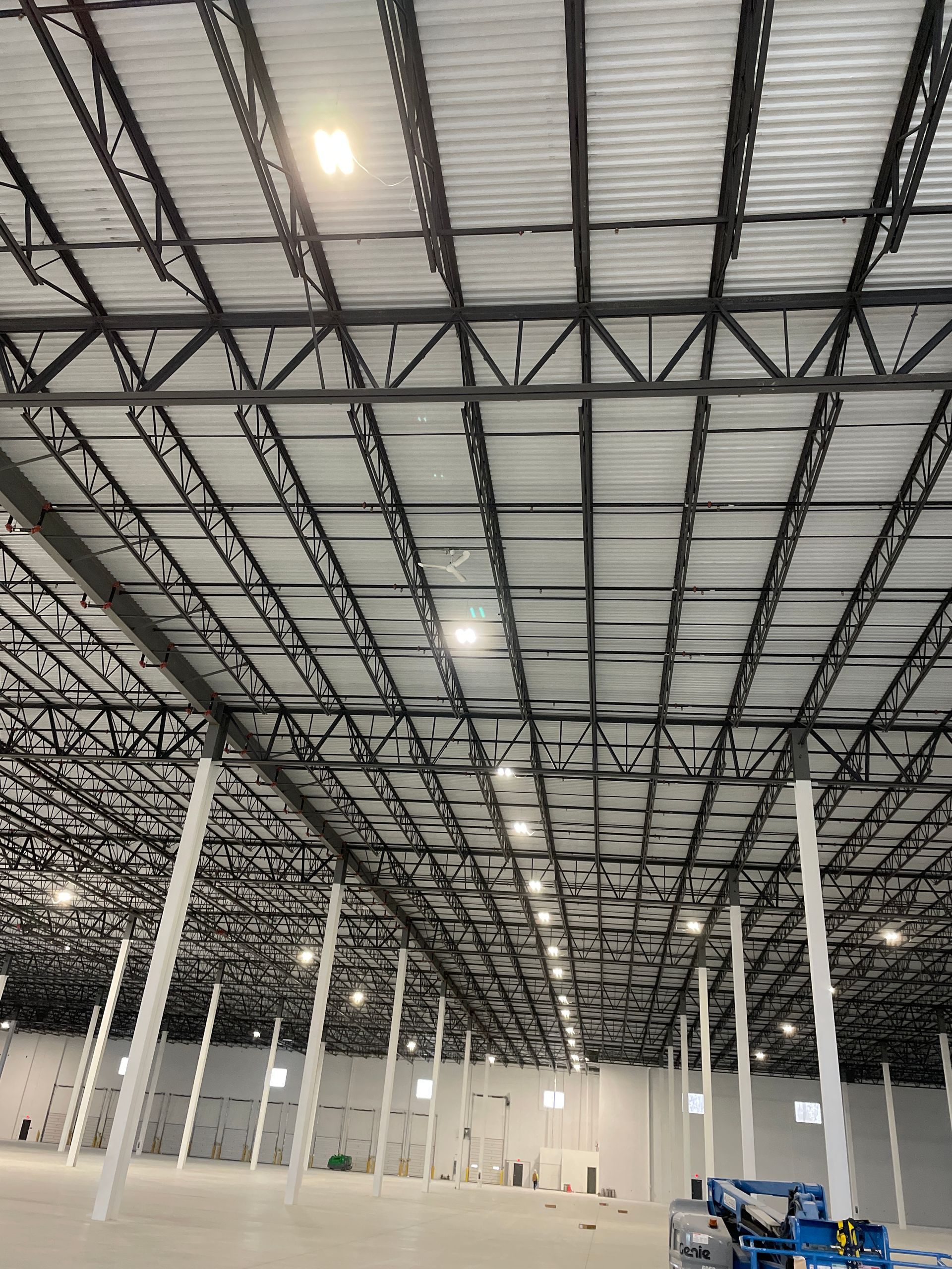 Interior of a large empty warehouse with a high ceiling, white columns, and industrial lighting.