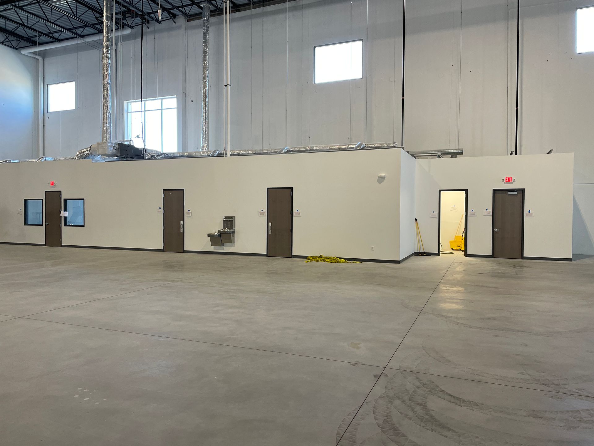 Industrial warehouse interior with a white office wall, several doors, and bright lights overhead