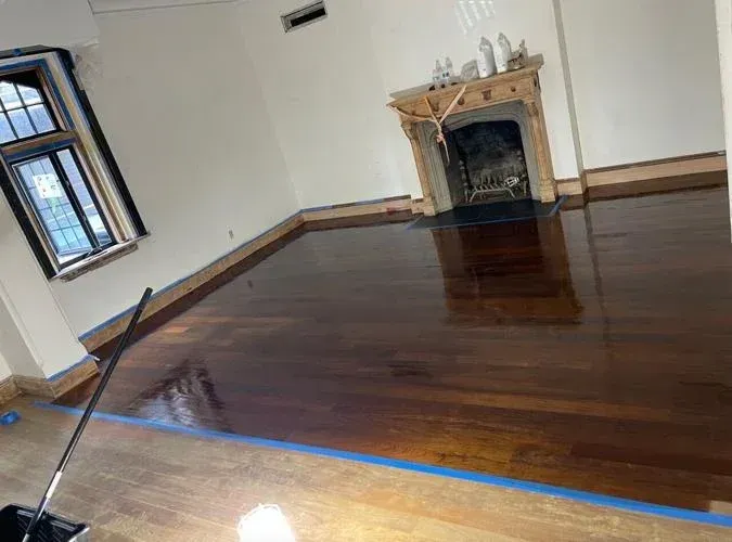 Newly stained hardwood floors with fireplace and window in a room.