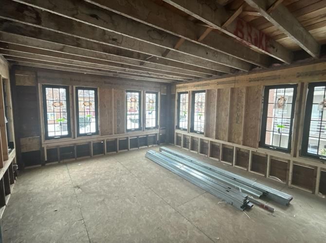 Room under renovation with exposed wood framing, windows, and construction materials on the floor.