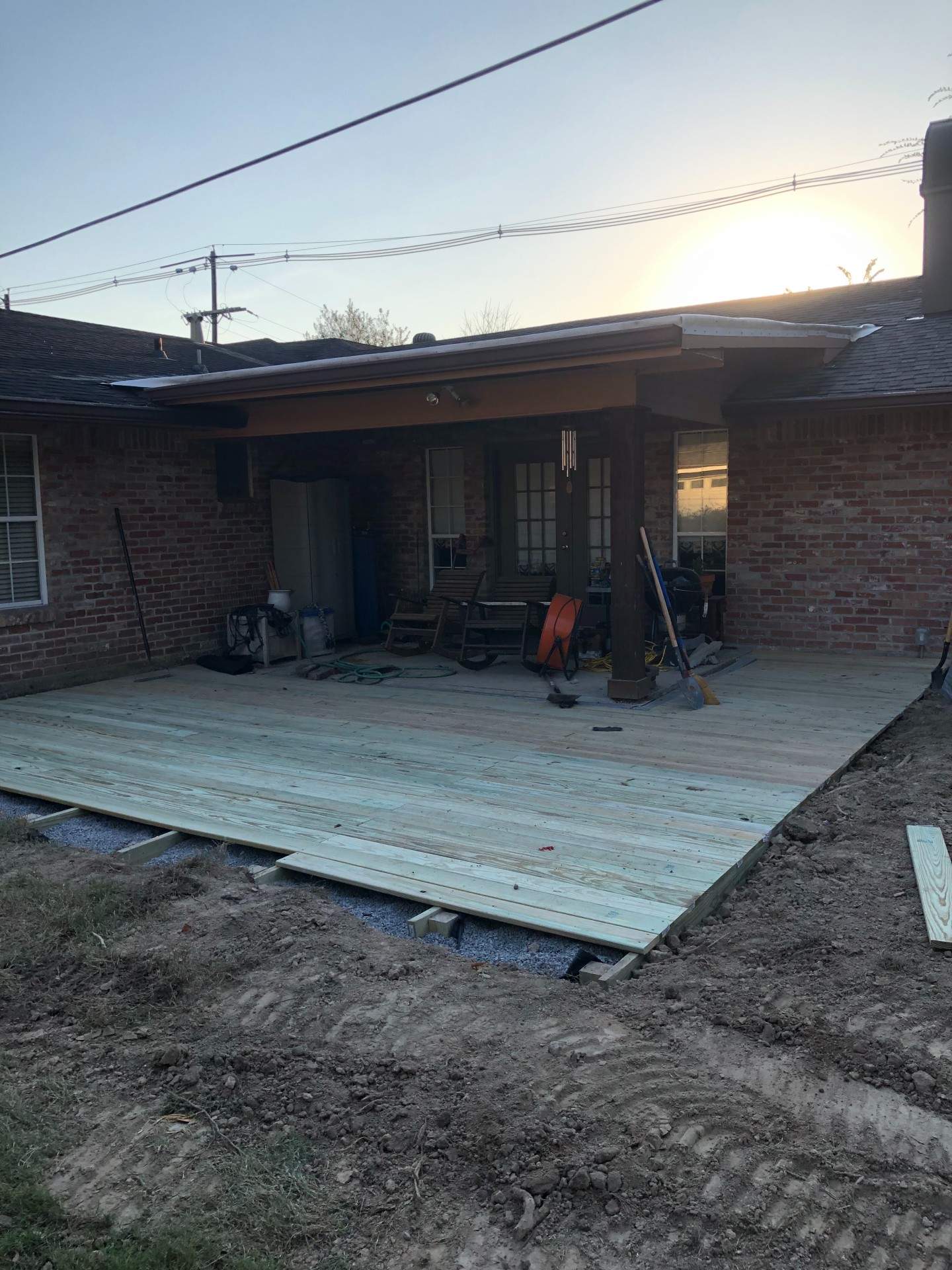 A partially built wooden deck outside a brick house. Construction tools are present. Overcast sky.