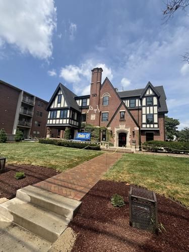 Brick building with Tudor style details, lush green lawn, and blue sky.