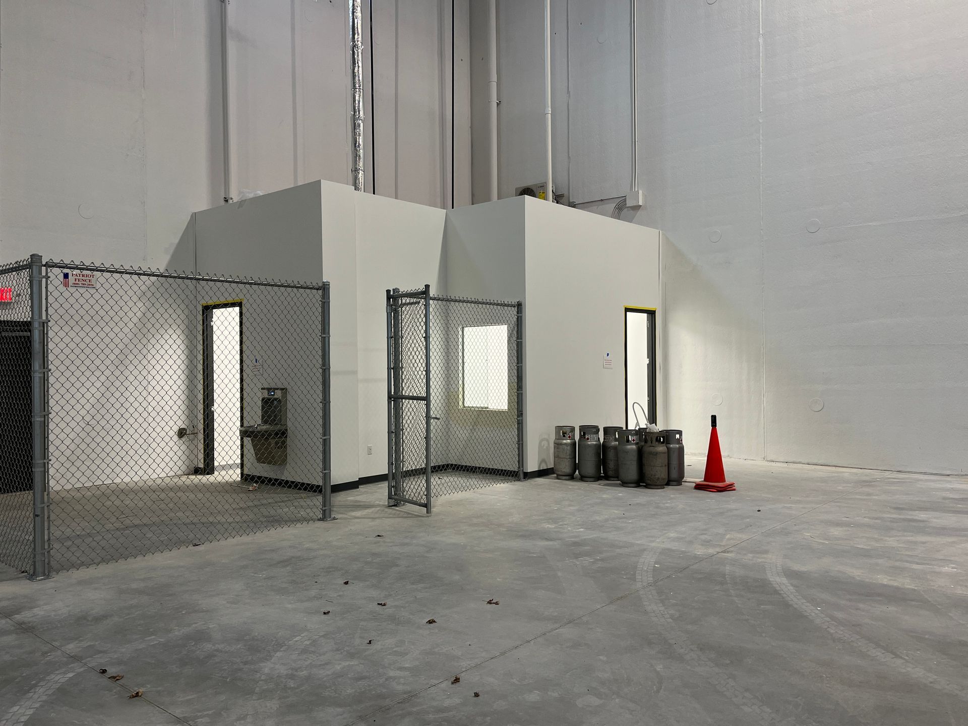 Empty industrial interior with gray concrete floor, fenced enclosures, and a red safety cone near the wall