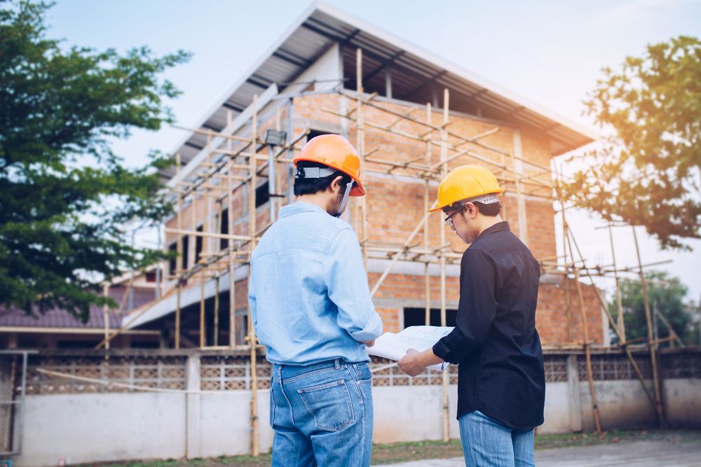 Two construction workers in hard hats reviewing blueprints at a building site.