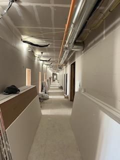Long, unfinished hallway in a building, with drywall and exposed pipes overhead.