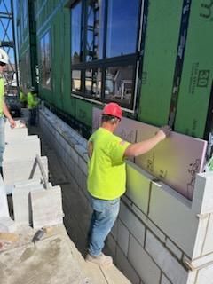 Construction worker in a hard hat installing pink insulation against a concrete wall. Green building wrap visible.