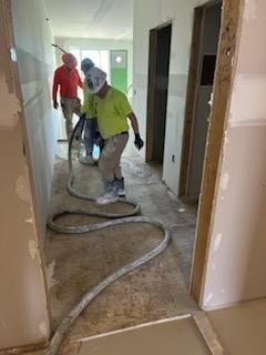 Workers applying material to a hallway floor. One wears a respirator, others wear work clothes, and a hose lies on the floor.