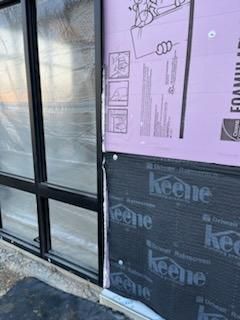 Exterior wall construction with black window frame, purple insulation, and black waterproof membrane.