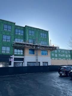 Building under construction with scaffolding; green siding, blue windows, gray sky.
