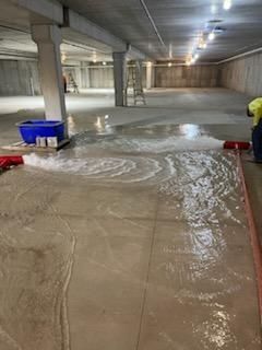 Flooded underground parking garage. Person using a squeegee to push water. Concrete floor and walls.