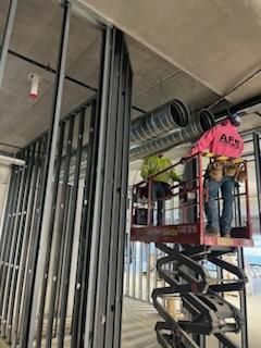 Construction workers on a lift installing ductwork, steel framing in unfinished building.