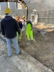 Construction workers wearing helmets and high-visibility clothing are working with equipment outdoors.