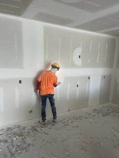 Construction worker taping drywall in a room with unfinished walls and floor.