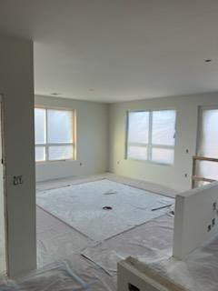Empty room under renovation with white walls, windows covered, and floor protection.