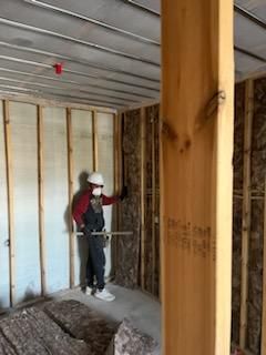 Construction worker installing insulation in a framed wall. Interior view of a building under construction.